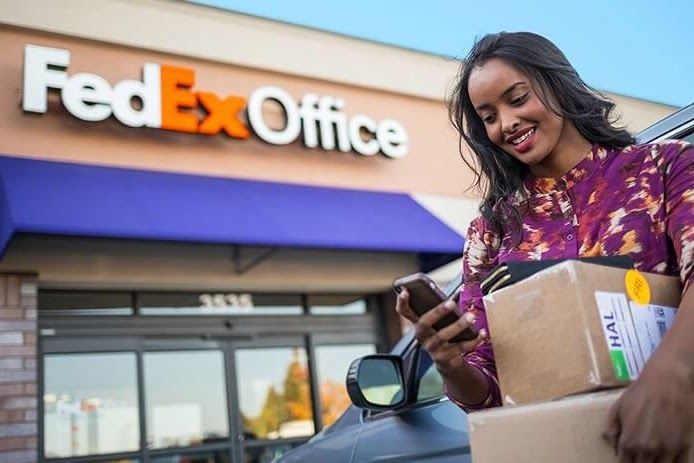 A person with shipping packages standing outside a FedEx Office