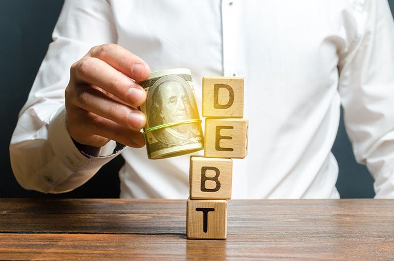 Man Knocks down the word tower of Debt with a bundle of dollars