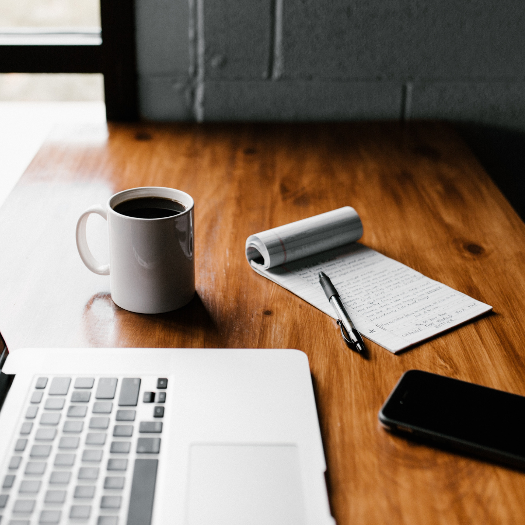 laptop, cup of coffee, and a ntepad with a pen