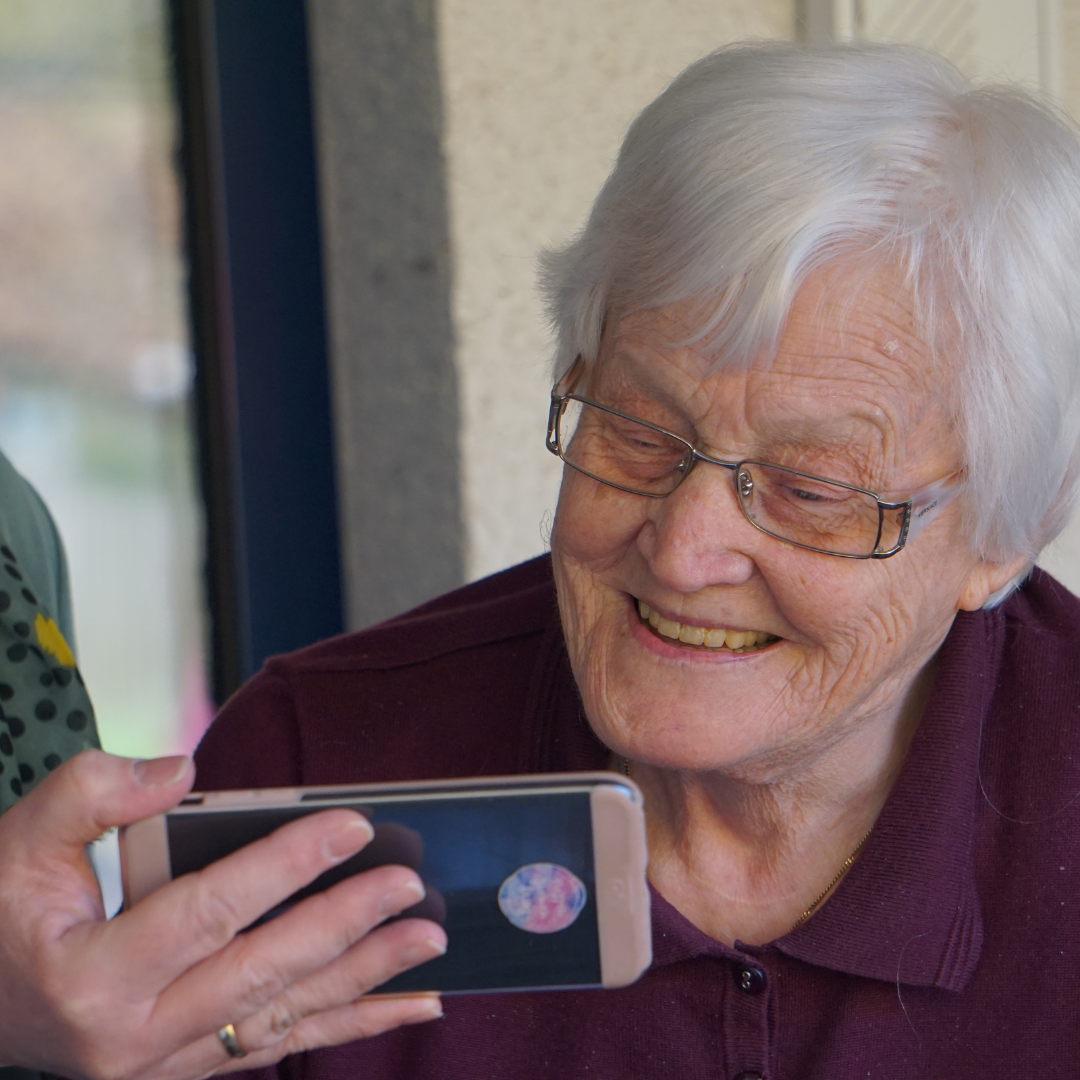 An old lady smiling and looking in the phone